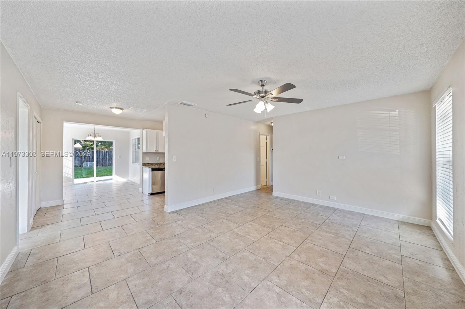 An empty living room with beige tile flooring, a ceiling fan, and an adjacent kitchen — 4721 NW 12th St, Lauderhill FL 33313, LAUDERHILL, FL