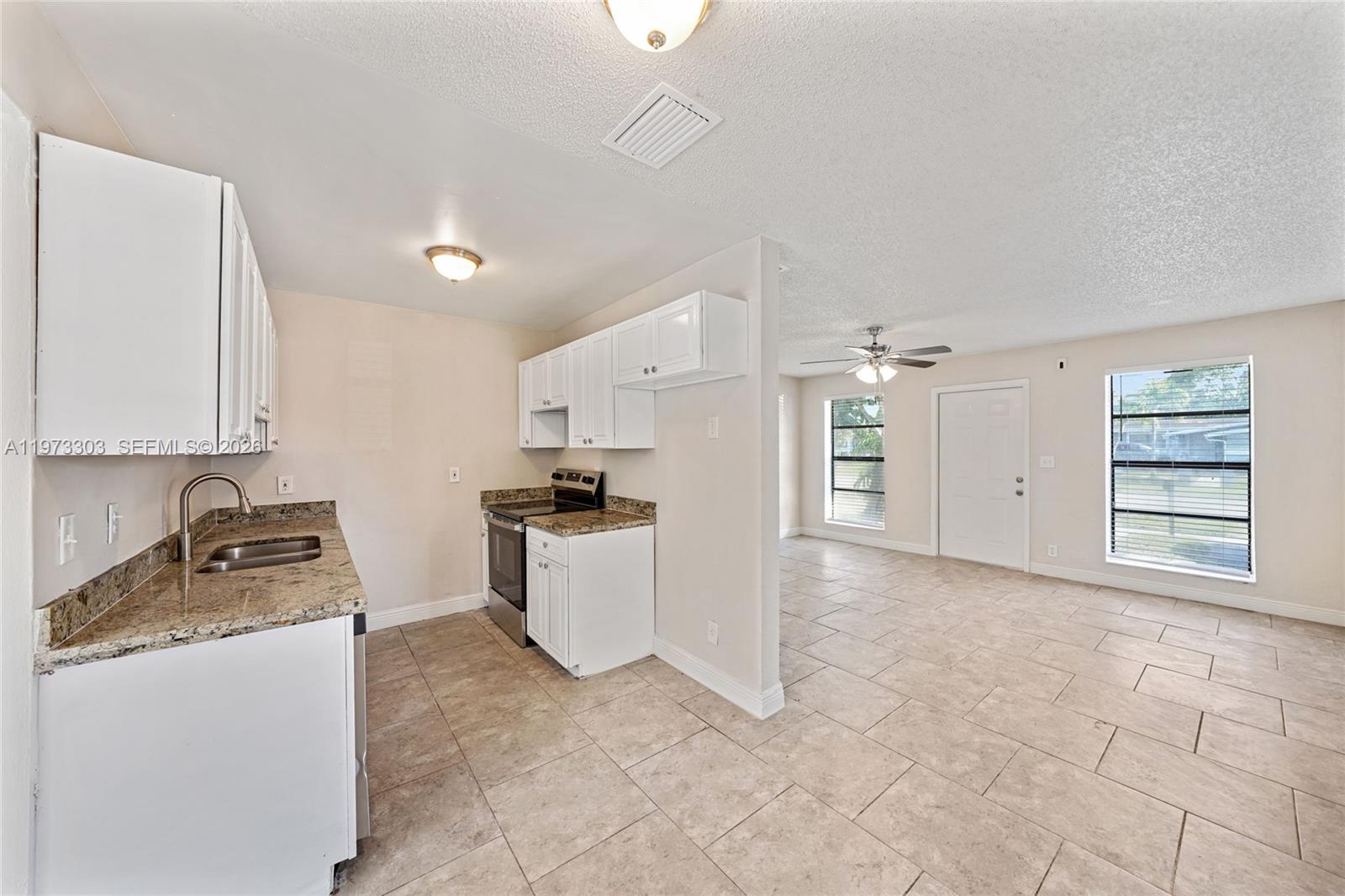 A kitchen with white cabinets and granite countertops opens into a tiled living area — 4721 NW 12th St, Lauderhill FL 33313, LAUDERHILL, FL