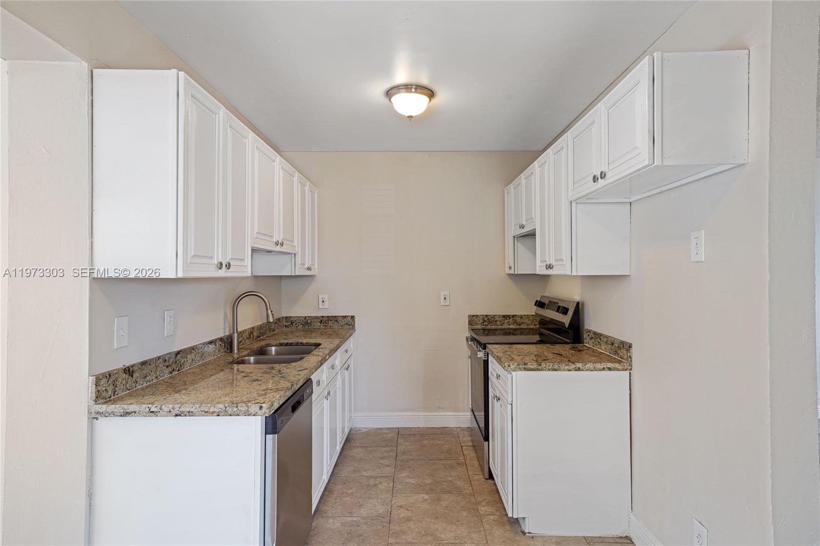 A galley kitchen features white cabinets, granite countertops, and stainless steel appliances — 4721 NW 12th St, Lauderhill FL 33313, LAUDERHILL, FL