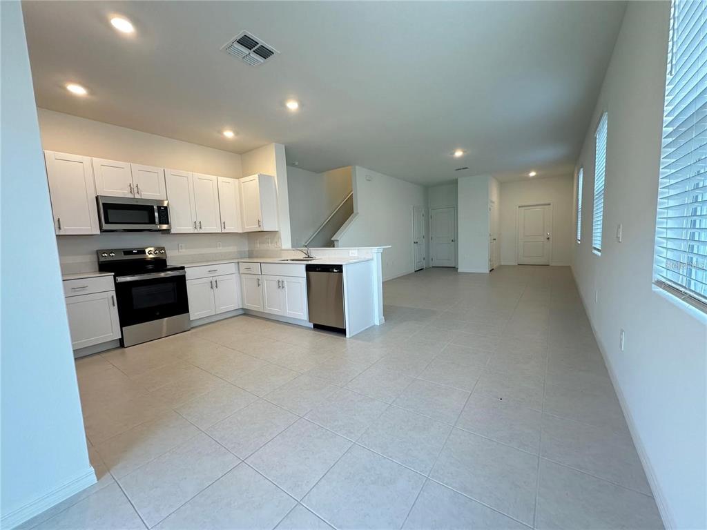 A kitchen with white cabinets and stainless steel appliances opens into a spacious tiled room — 2655 BUTTERCUP LUCINE LANE, RUSKIN, FL