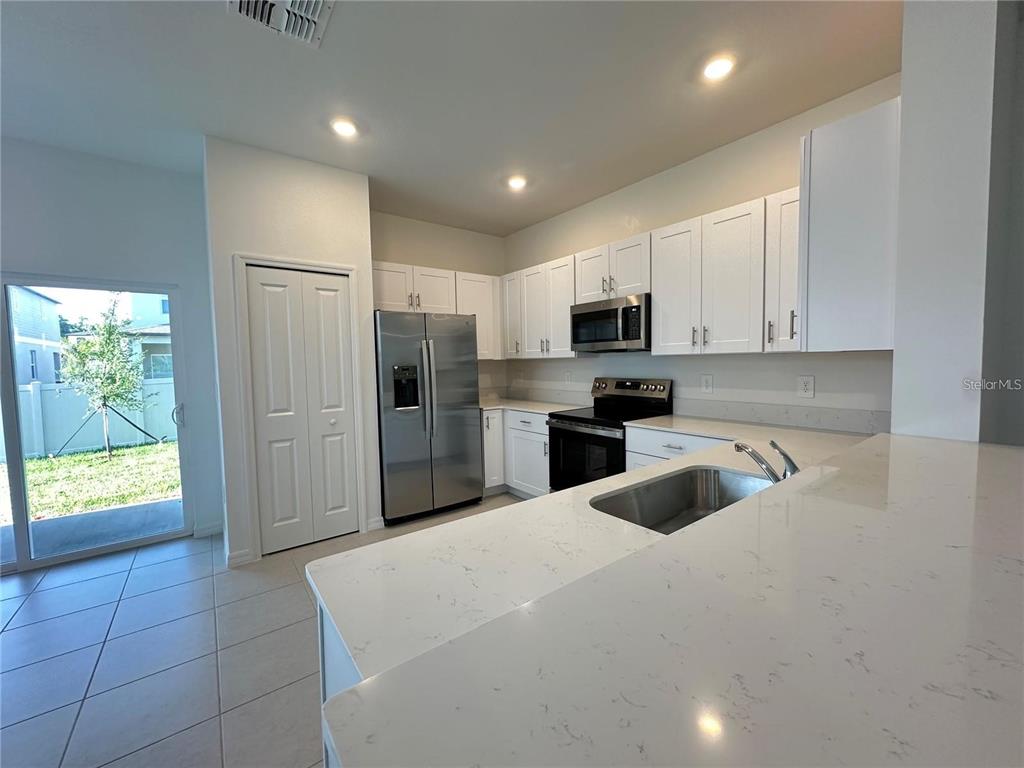 A kitchen features white cabinets, stainless steel appliances, quartz countertops, and a sliding glass door — 2655 BUTTERCUP LUCINE LANE, RUSKIN, FL