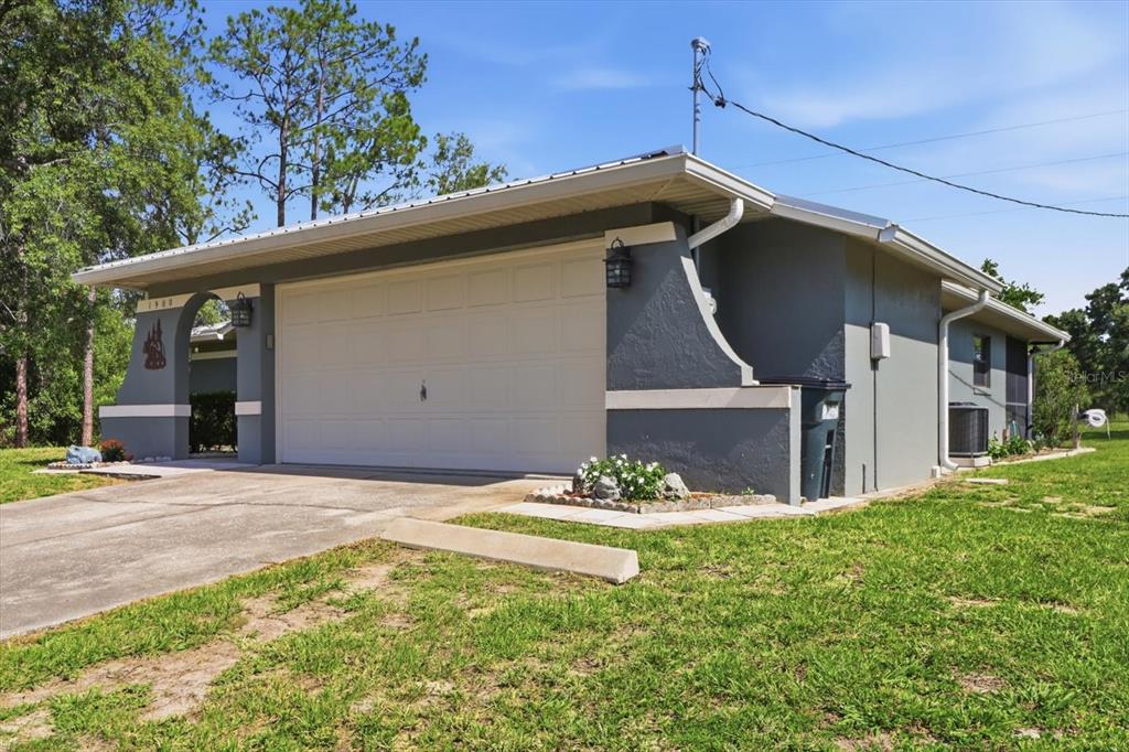 A gray house exterior features a white garage door, a concrete driveway, and landscaping — 1900 W ALHAMBRA DRIVE, CITRUS SPRINGS, FL
