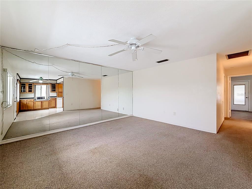 A carpeted room features a large mirrored wall reflecting an adjacent kitchen with wooden cabinets — 8101 113TH STREET UNIT 309, SEMINOLE, FL