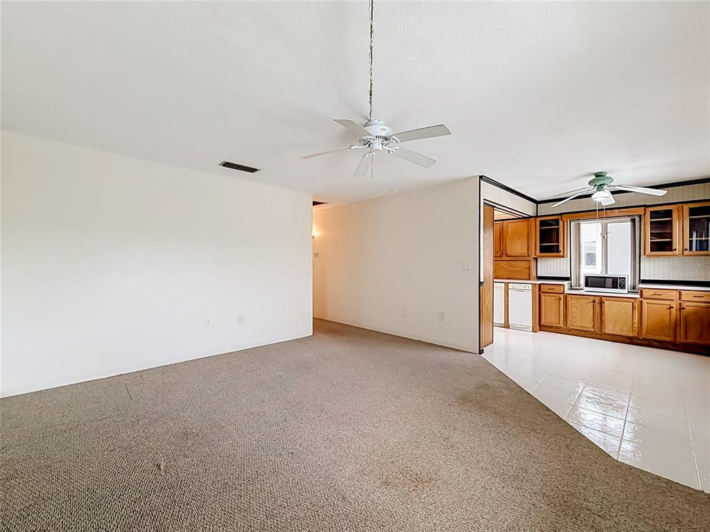 A living room with beige carpet transitions into a kitchen with wood cabinets and tile — 8101 113TH STREET UNIT 309, SEMINOLE, FL