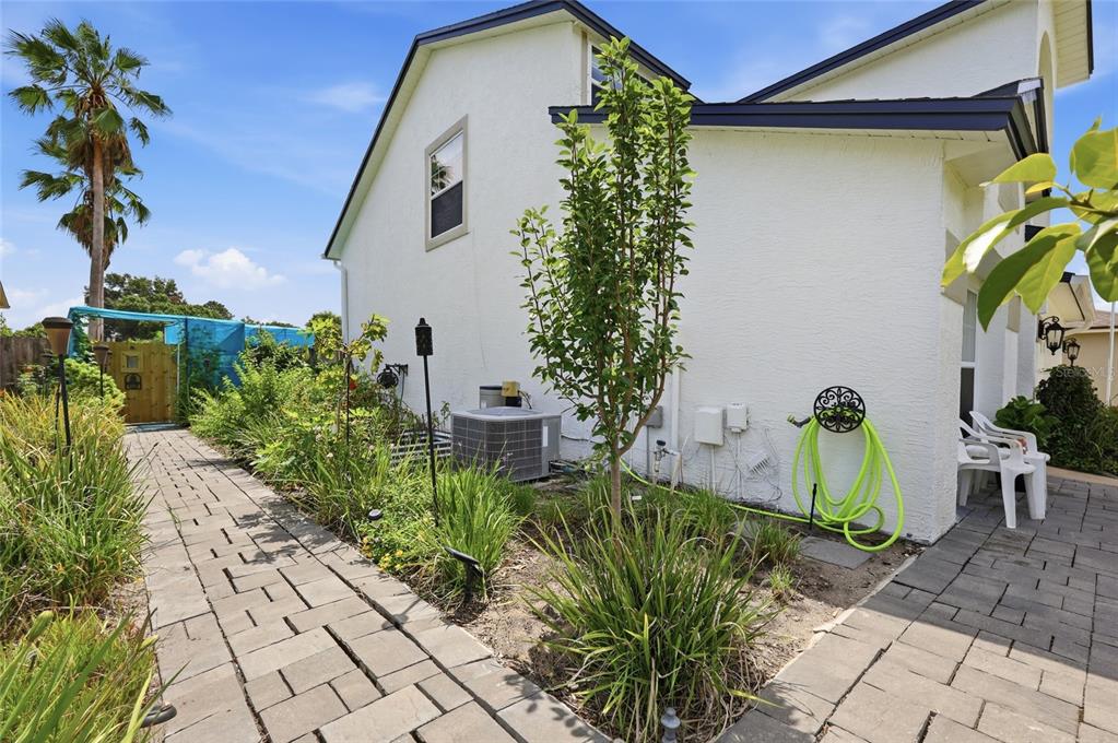 A paved walkway leads past a white house exterior with landscaping, an air conditioning unit, and hose — 2909 SOMERSWORTH COURT, ORLANDO, FL