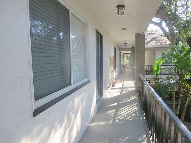 An outdoor apartment walkway with a large window, a door, and a black metal railing — 3914 W NEPTUNE STREET UNIT 27, TAMPA, FL