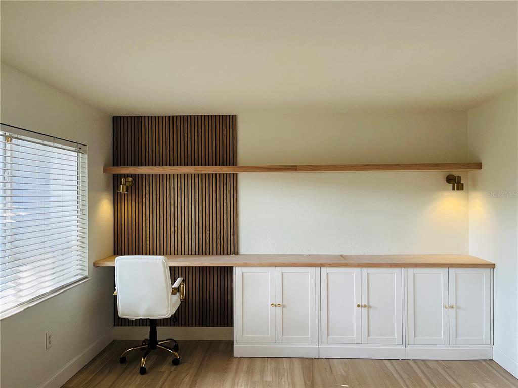 A home office features a long wooden desk, white base cabinets, and a slatted wood accent wall — 3914 W NEPTUNE STREET UNIT 27, TAMPA, FL