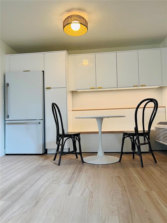 A kitchen features white cabinetry, a refrigerator, a dining table with two chairs, and wood-look flooring — 3914 W NEPTUNE STREET UNIT 27, TAMPA, FL