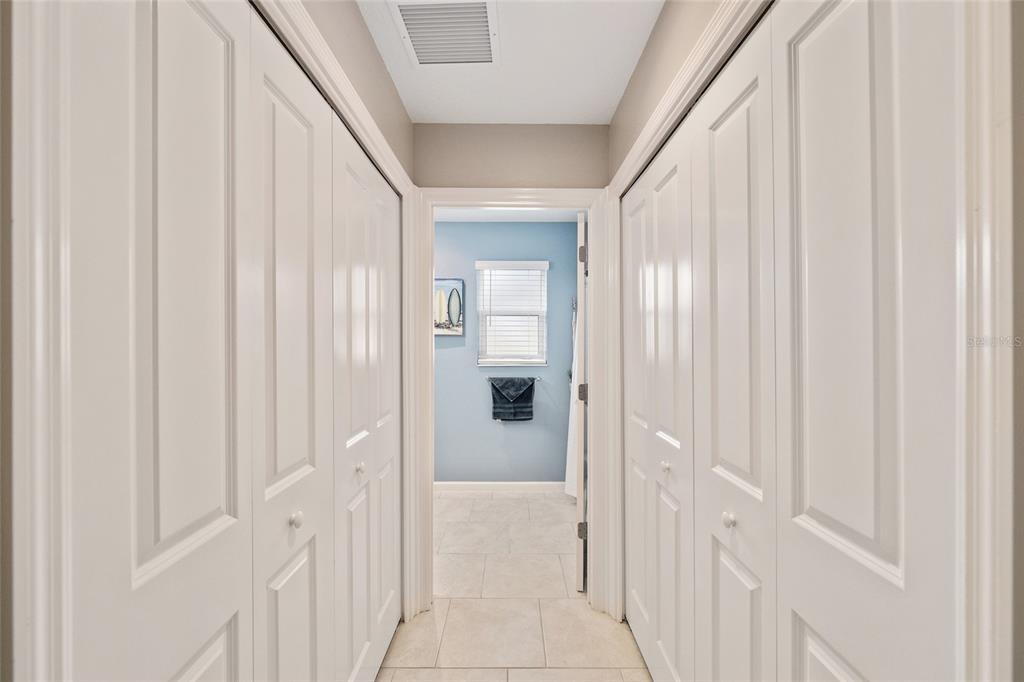A hallway with white bi-fold closet doors on both sides leads into a blue bathroom — 1442 JOSHUA COURT, THE VILLAGES, FL