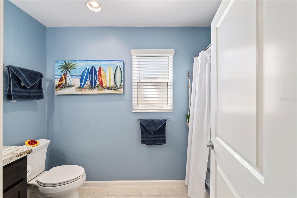 A bathroom with blue walls, a toilet, a shower curtain, and a surfboard wall art piece — 1442 JOSHUA COURT, THE VILLAGES, FL