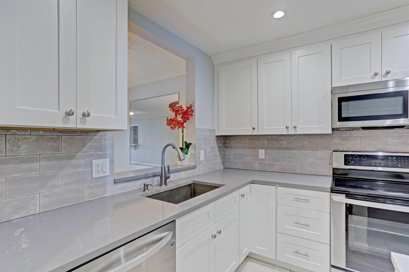 A kitchen features white cabinets, gray subway tile backsplash, stainless steel appliances, and quartz countertops — 3011 SW 21st Terrace # 382a, Delray Beach FL 33445, DELRAY BEACH, FL