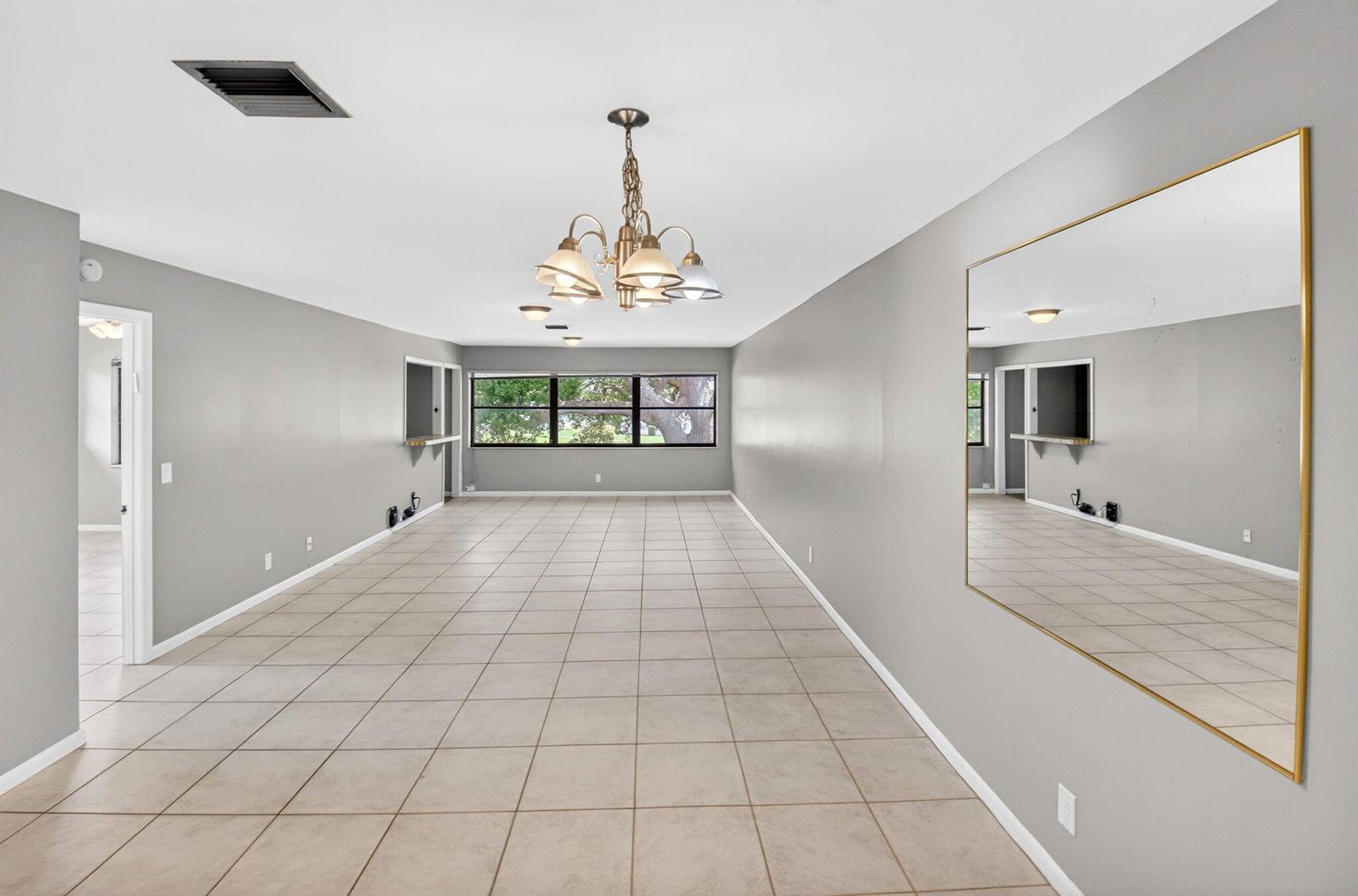 A long, empty room features gray walls, light-colored tile flooring, a chandelier, and a mirror — 3011 SW 21st Terrace # 382a, Delray Beach FL 33445, DELRAY BEACH, FL