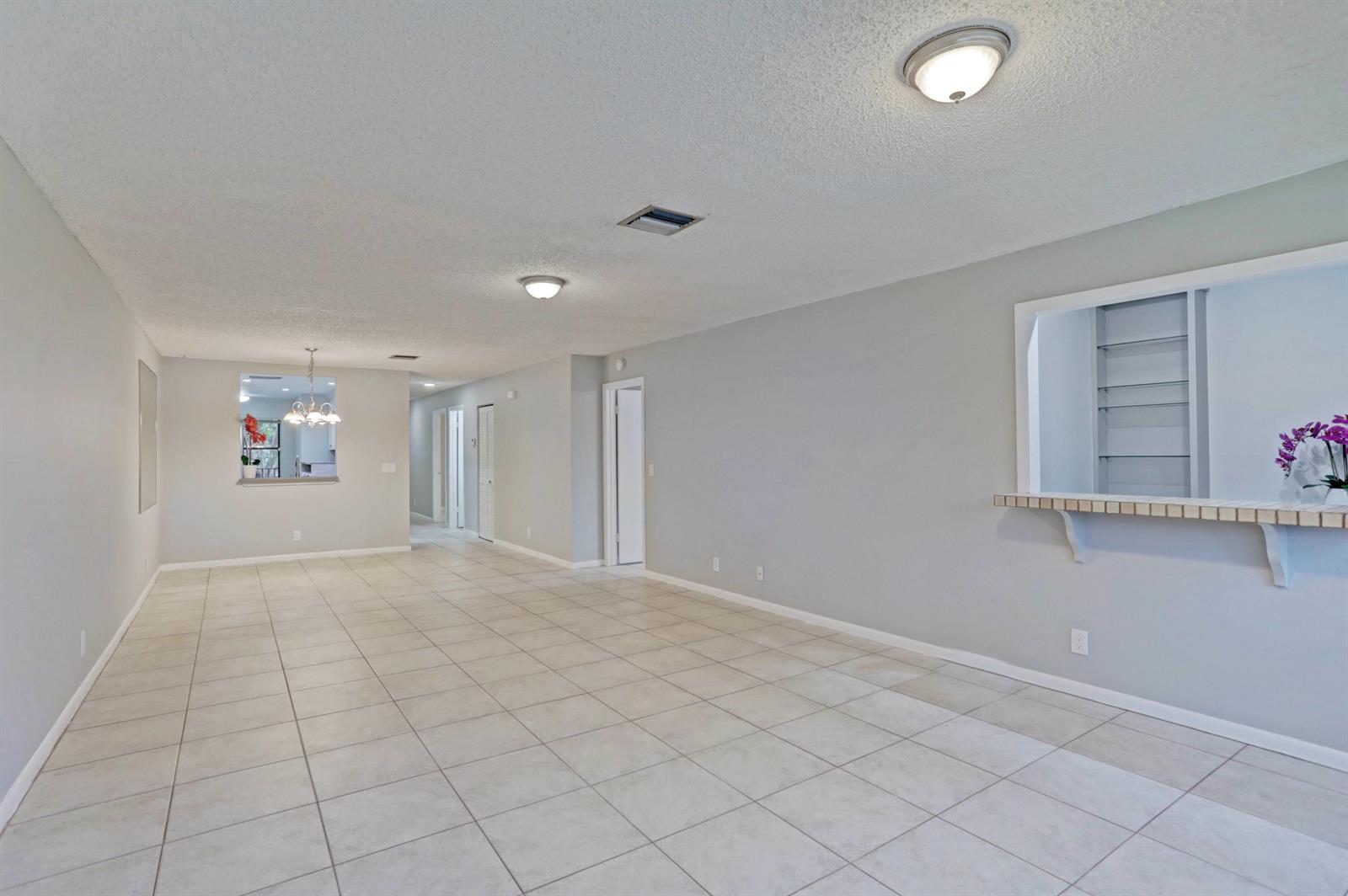 An open-concept living area features light gray walls, large beige floor tiles, and two pass-through windows — 3011 SW 21st Terrace # 382a, Delray Beach FL 33445, DELRAY BEACH, FL