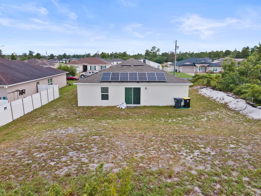 A rear view of a single-story house with solar panels on the roof and yard — 27 MAGNOLIA BLOSSOM LANE, KISSIMMEE, FL