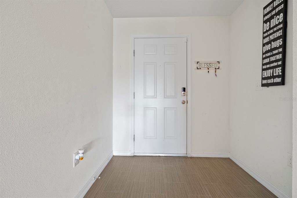 An entryway features a white door, wood-look tile flooring, and a wall-mounted sign — 27 MAGNOLIA BLOSSOM LANE, KISSIMMEE, FL