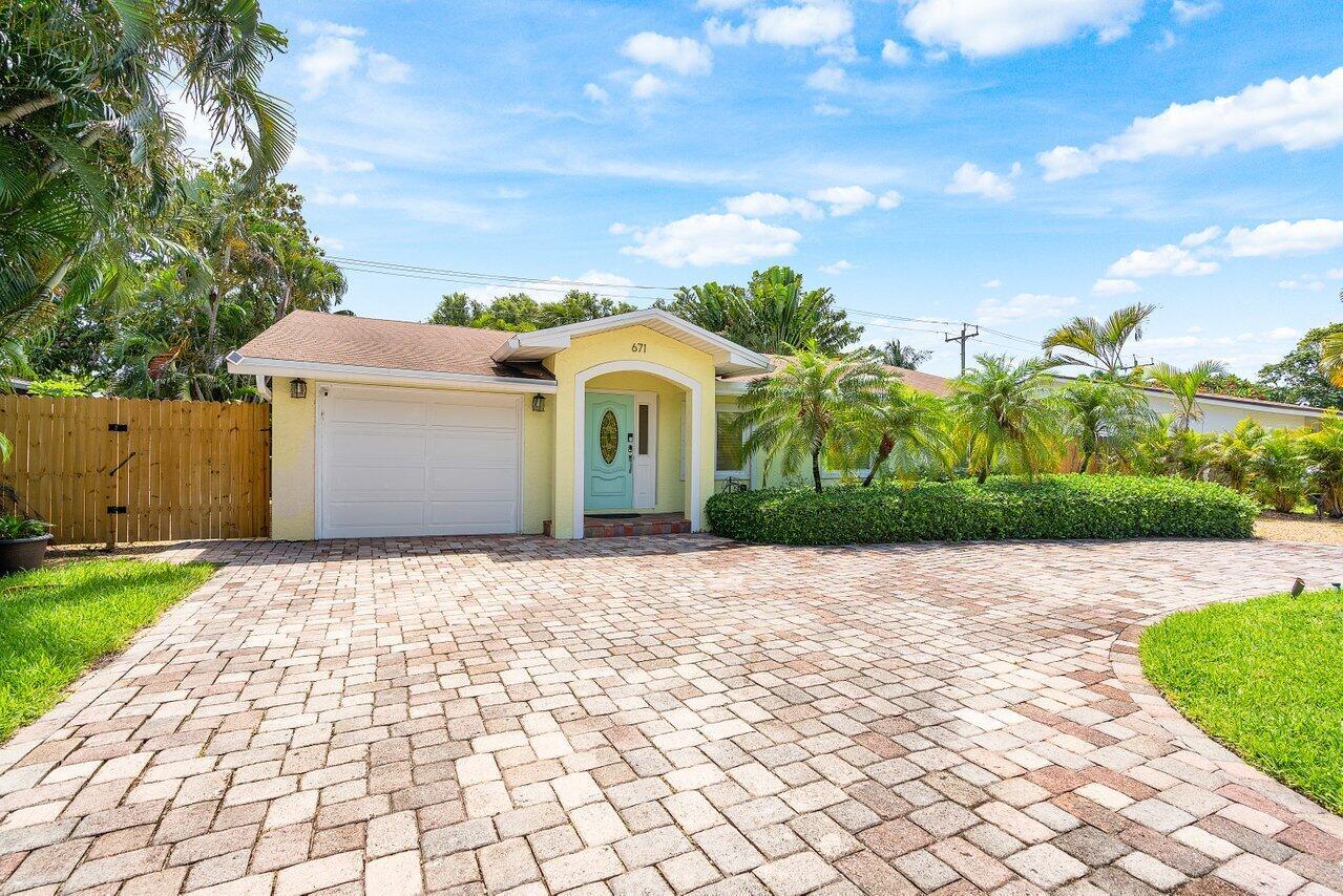 A single-story yellow house features a paved driveway, a white garage door, and a turquoise door — 671 Lindell Boulevard, Delray Beach FL 33444, DELRAY BEACH, FL