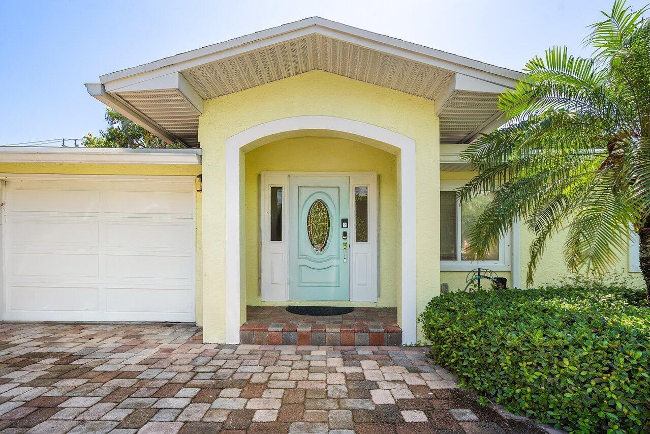 A light yellow house exterior features a pale blue front door and a brick driveway — 671 Lindell Boulevard, Delray Beach FL 33444, DELRAY BEACH, FL