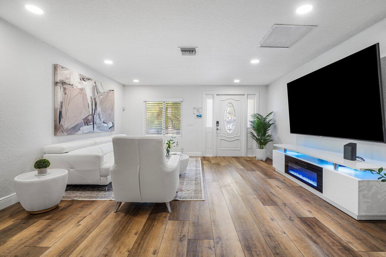 A modern living room features white furniture, a large television, and wood-look flooring — 671 Lindell Boulevard, Delray Beach FL 33444, DELRAY BEACH, FL