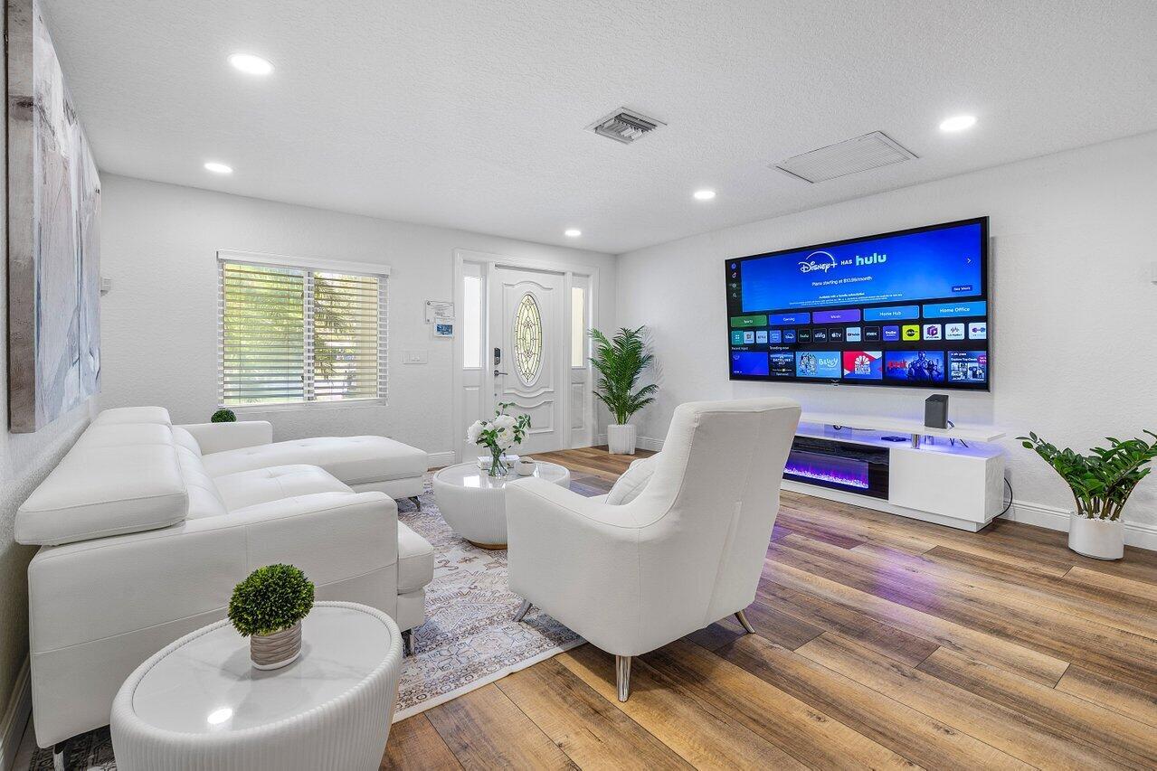 A modern living room features a white sectional sofa, armchair, and a wall-mounted television — 671 Lindell Boulevard, Delray Beach FL 33444, DELRAY BEACH, FL