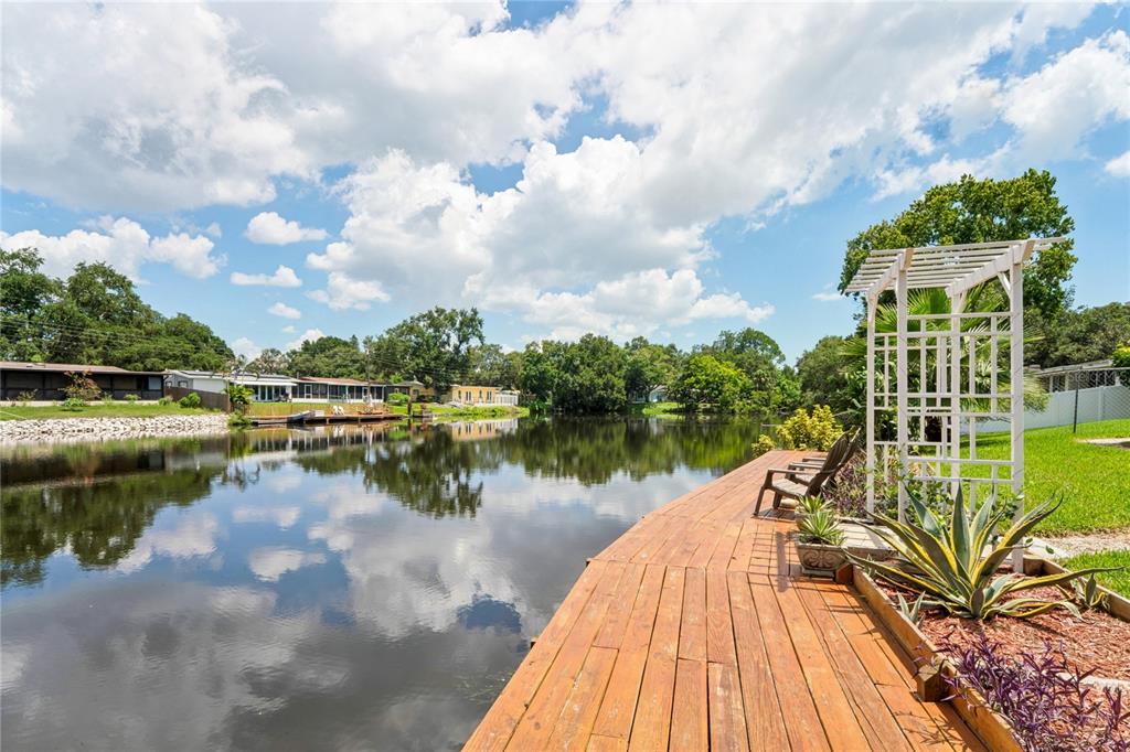 A wooden deck with a white arbor overlooks a calm lake under a cloudy sky — 10681 SEMINOLE FOREST STREET E, SEMINOLE, FL
