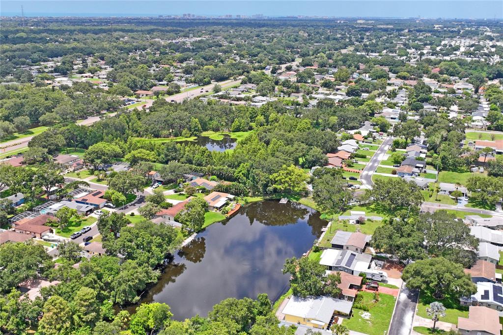 An aerial view shows a residential neighborhood surrounding a central pond with dense tree cover — 10681 SEMINOLE FOREST STREET E, SEMINOLE, FL