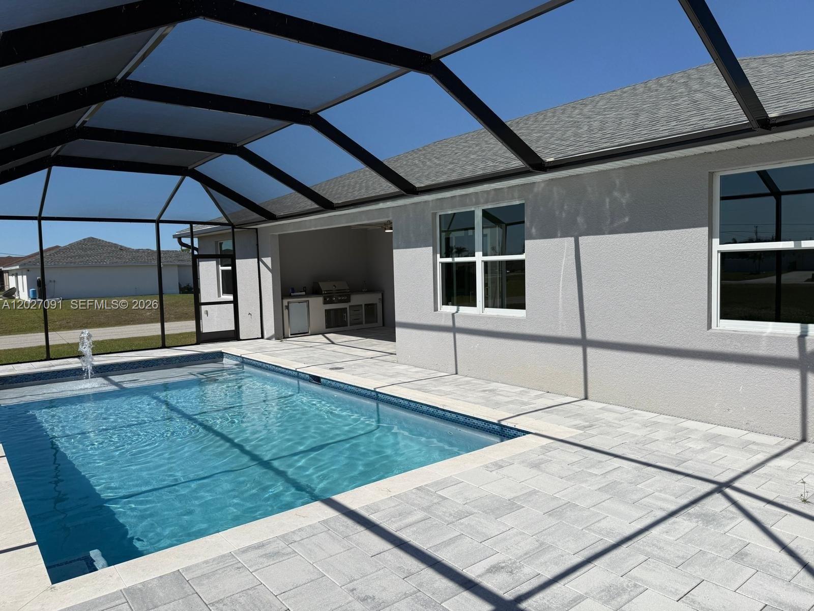 A swimming pool with a fountain sits inside a screened enclosure next to a patio — 314 NW 16, Cape Coral FL 33993, CAPE CORAL, FL