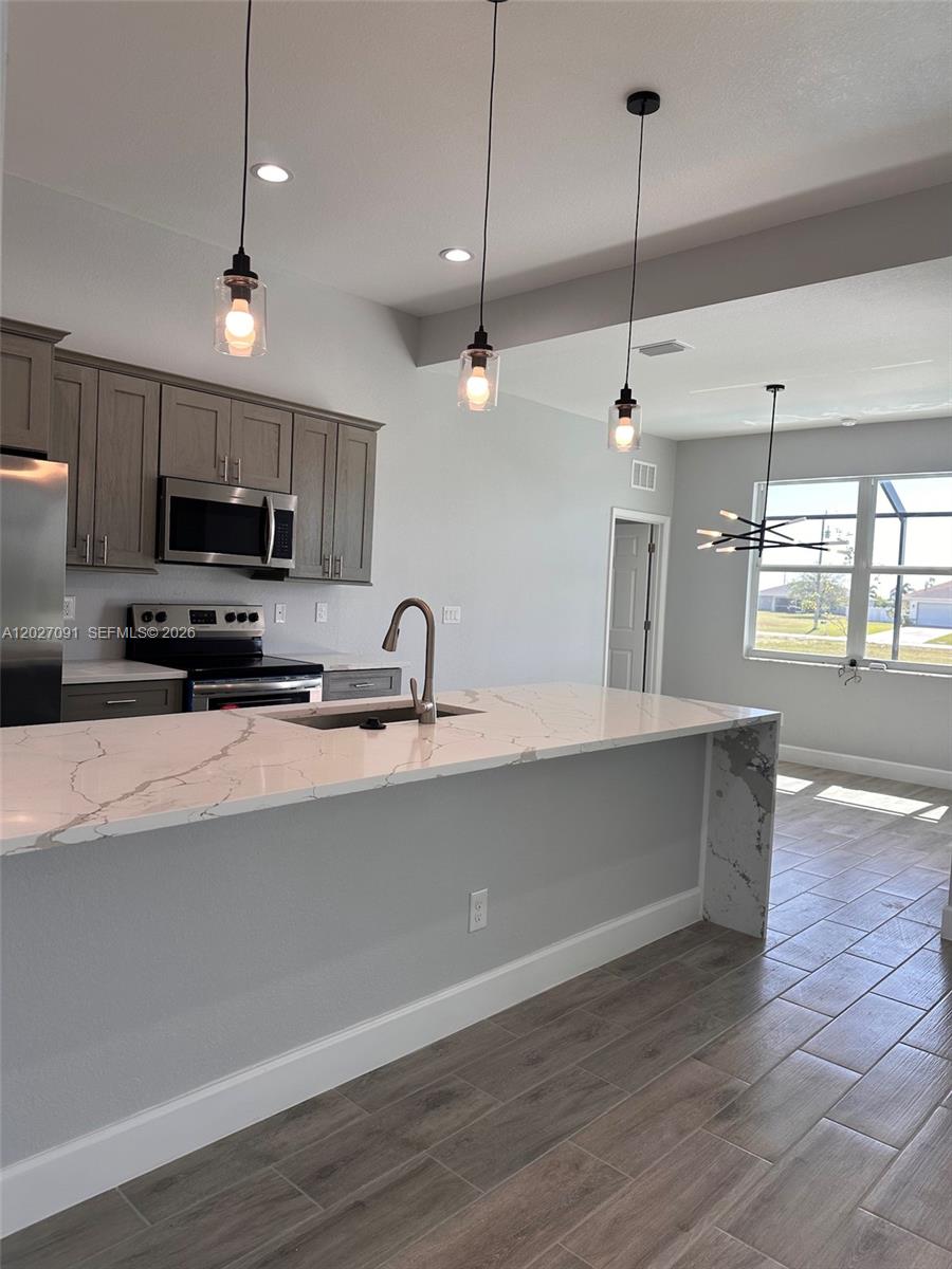 A kitchen features gray cabinets, a white marble-look island, and pendant lighting — 314 NW 16, Cape Coral FL 33993, CAPE CORAL, FL