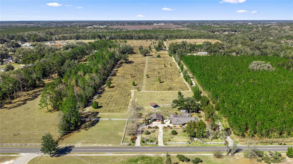 An aerial view shows a house with a large yard and pasture bordered by trees — 873 SW TROY STREET, LAKE CITY, FL