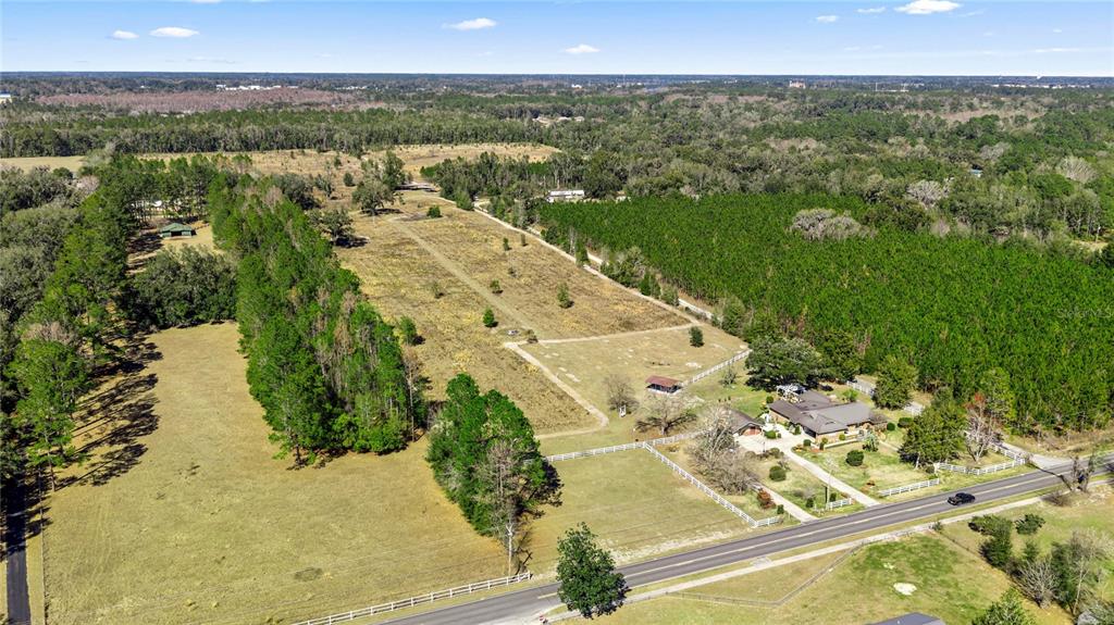 An aerial view shows a rural property with a house, pastures, and surrounding wooded areas — 873 SW TROY STREET, LAKE CITY, FL