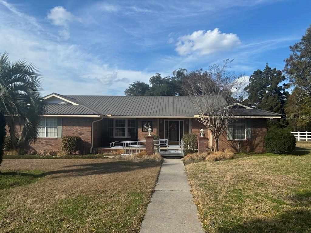 A single-story brick house with a metal roof and a wheelchair ramp at the entrance — 873 SW TROY STREET, LAKE CITY, FL