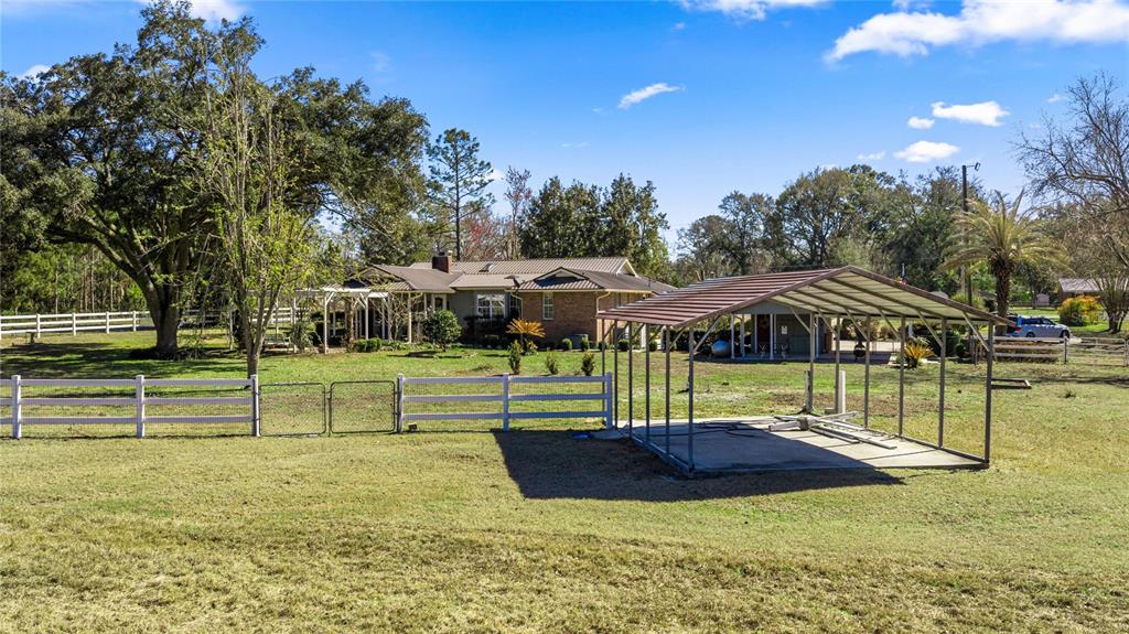 A rural property features a house, a metal carport, and white fencing on a grassy lot — 873 SW TROY STREET, LAKE CITY, FL