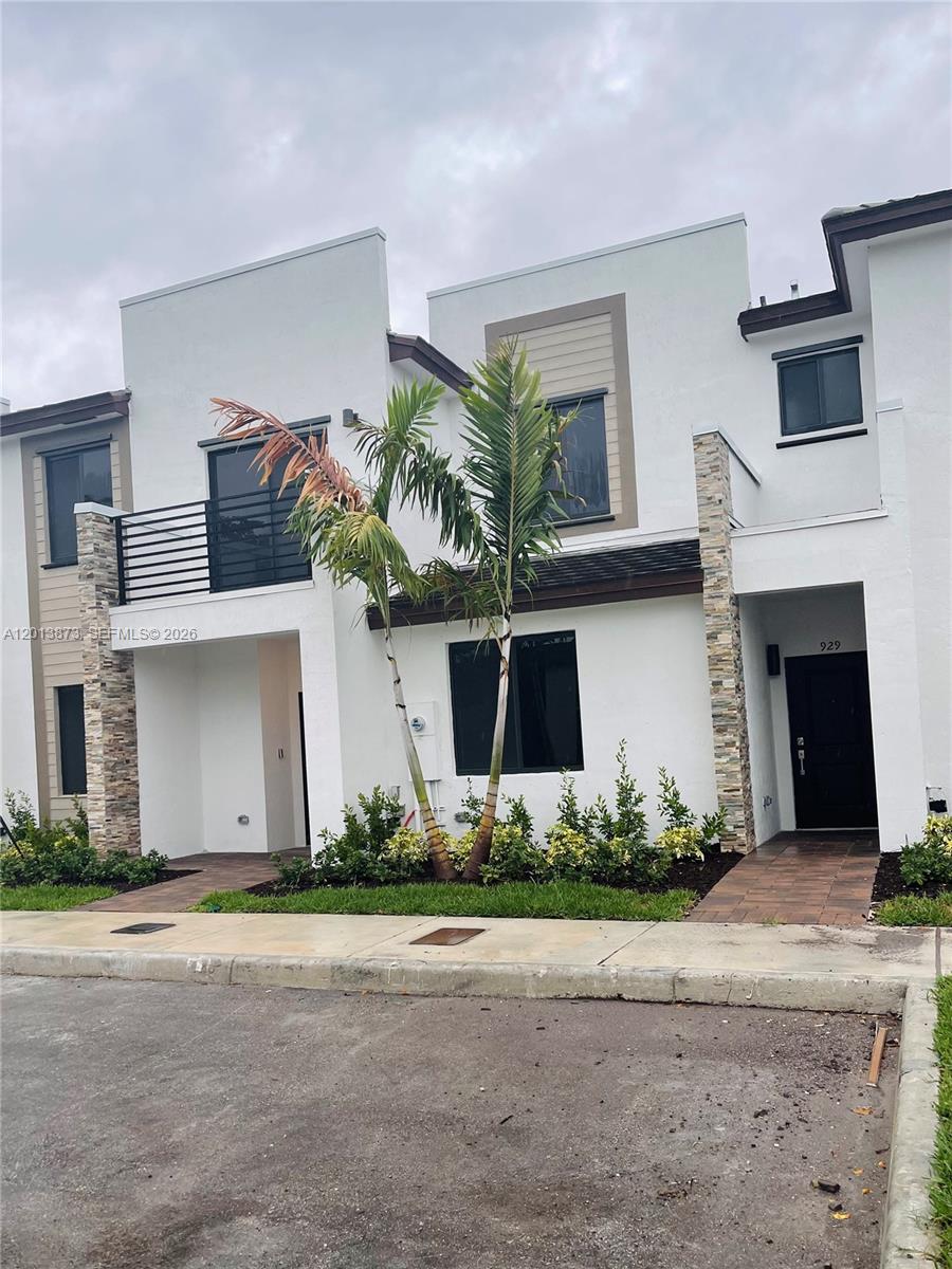 A two-story townhouse exterior features white stucco walls, stone accents, and a small palm tree — 929 NE 211th St, Miami FL 33179, MIAMI, FL