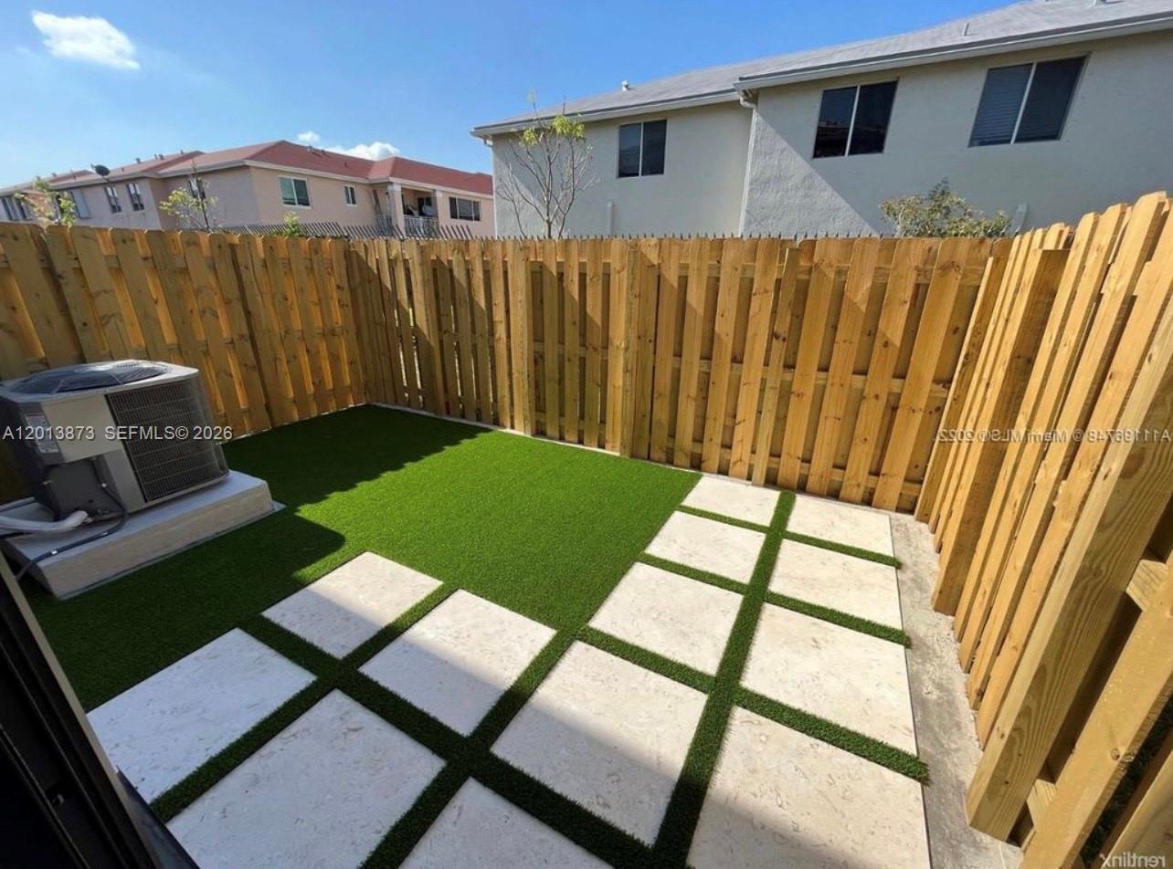 A small fenced backyard features artificial turf, square stone pavers, and an air conditioning unit — 929 NE 211th St, Miami FL 33179, MIAMI, FL