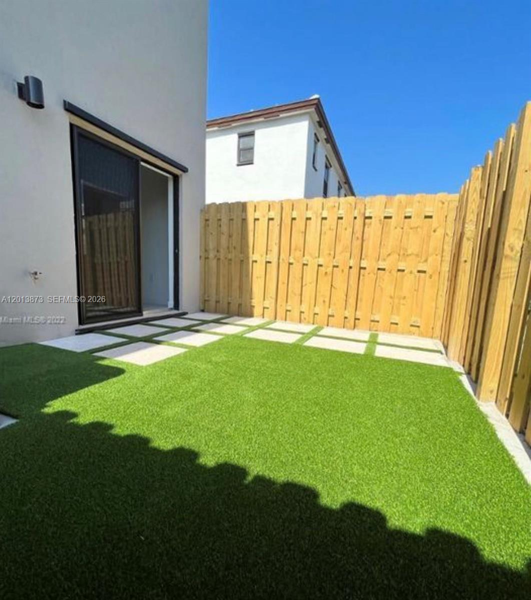A small backyard features artificial turf, square concrete pavers, and a wooden privacy fence — 929 NE 211th St, Miami FL 33179, MIAMI, FL