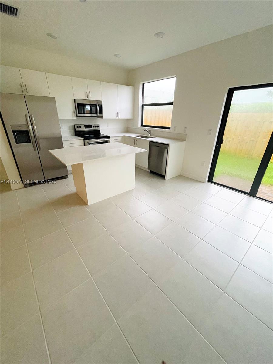 A modern kitchen features white cabinets, stainless steel appliances, a center island, and tile flooring — 929 NE 211th St, Miami FL 33179, MIAMI, FL