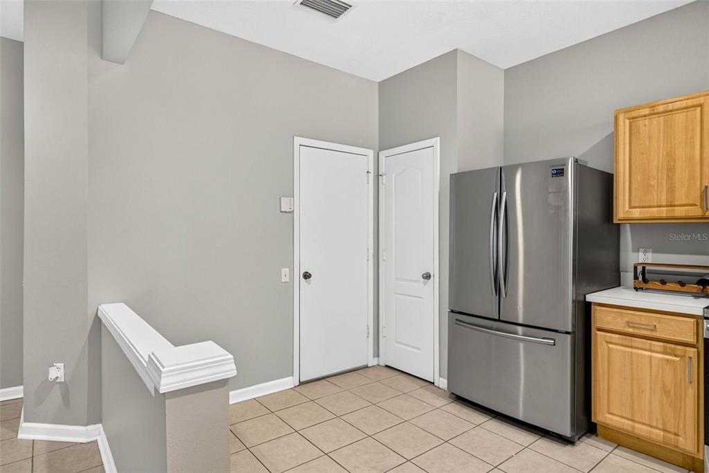 A kitchen area features light gray walls, tile flooring, a stainless steel refrigerator, and wood cabinets — 26624 CHIMNEY SPIRE LANE, WESLEY CHAPEL, FL