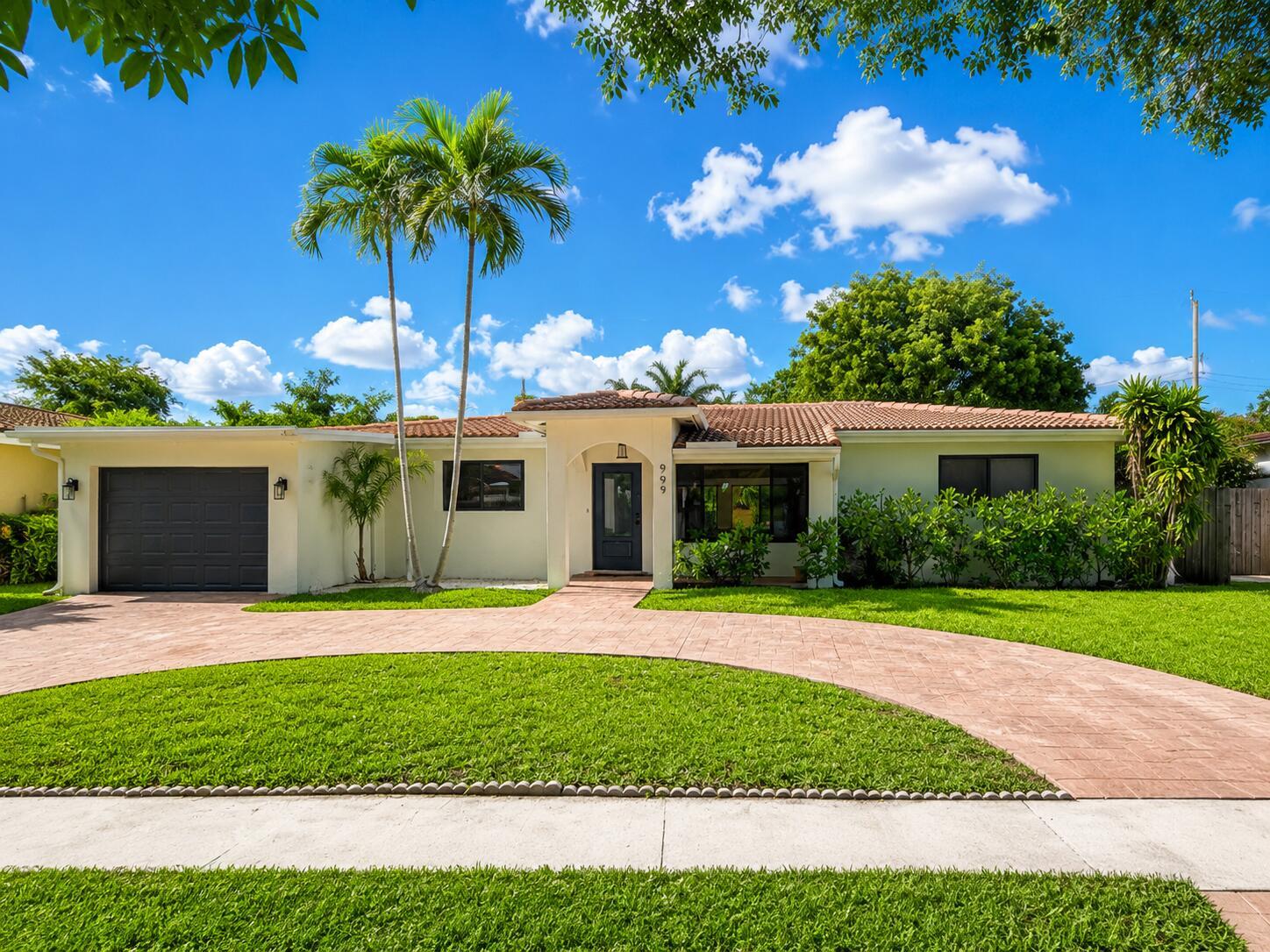 A single-story house with a circular brick driveway, palm trees, and a dark front door — 909 SE 14th Drive, Deerfield Beach FL 33441, DEERFIELD BEACH, FL