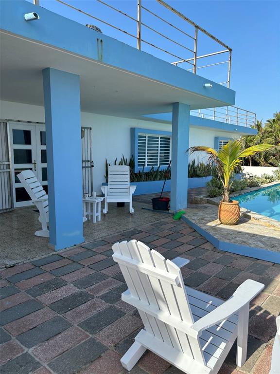 A patio with white Adirondack chairs overlooks a swimming pool next to a blue house — 681 N KM 11.7 ISLOTE, ARECIBO, PR