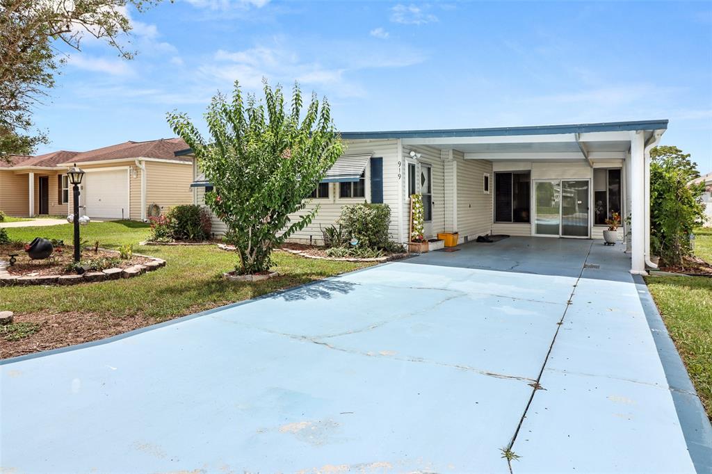 A single-story house with light siding, a blue-painted driveway, and a covered carport — 919 WEEPING WILLOW AVENUE, LADY LAKE, FL