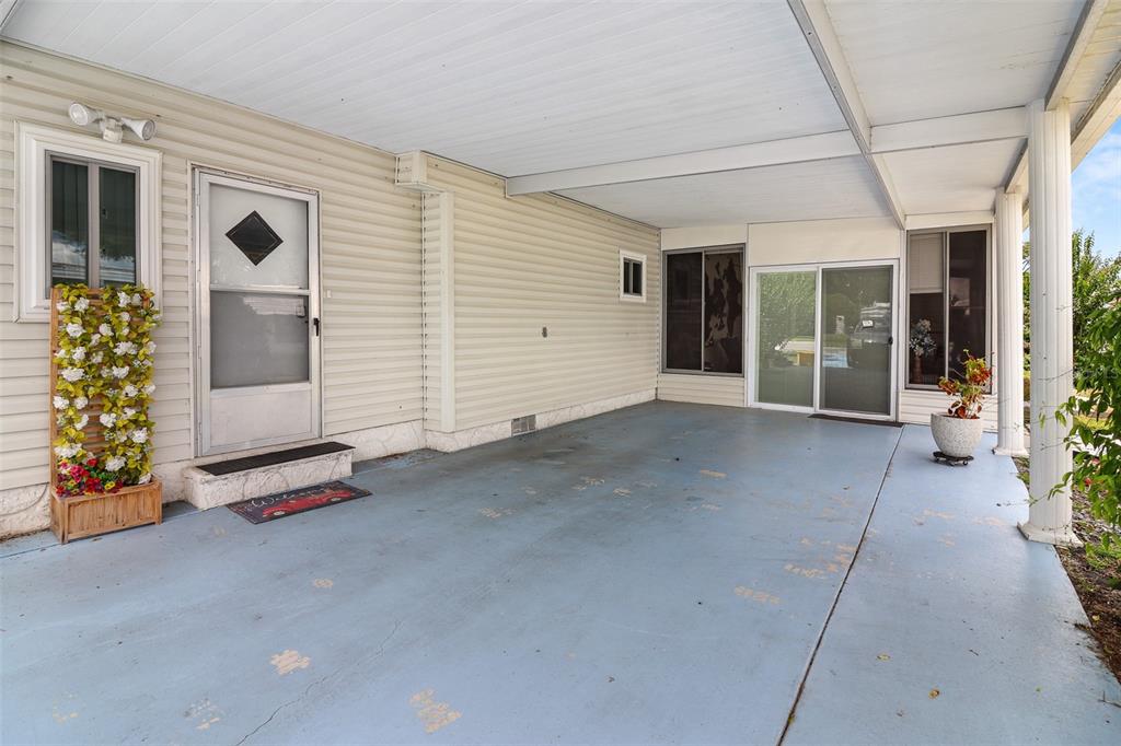 A covered carport with light blue concrete flooring, beige siding, and a glass sliding door — 919 WEEPING WILLOW AVENUE, LADY LAKE, FL