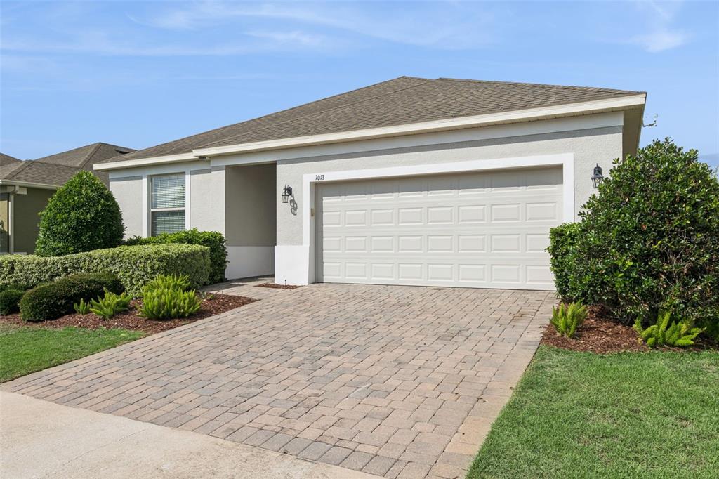 A single-story house with a beige stucco exterior, a two-car garage, and a paver driveway — 1013 SADIE RIDGE ROAD, CLERMONT, FL