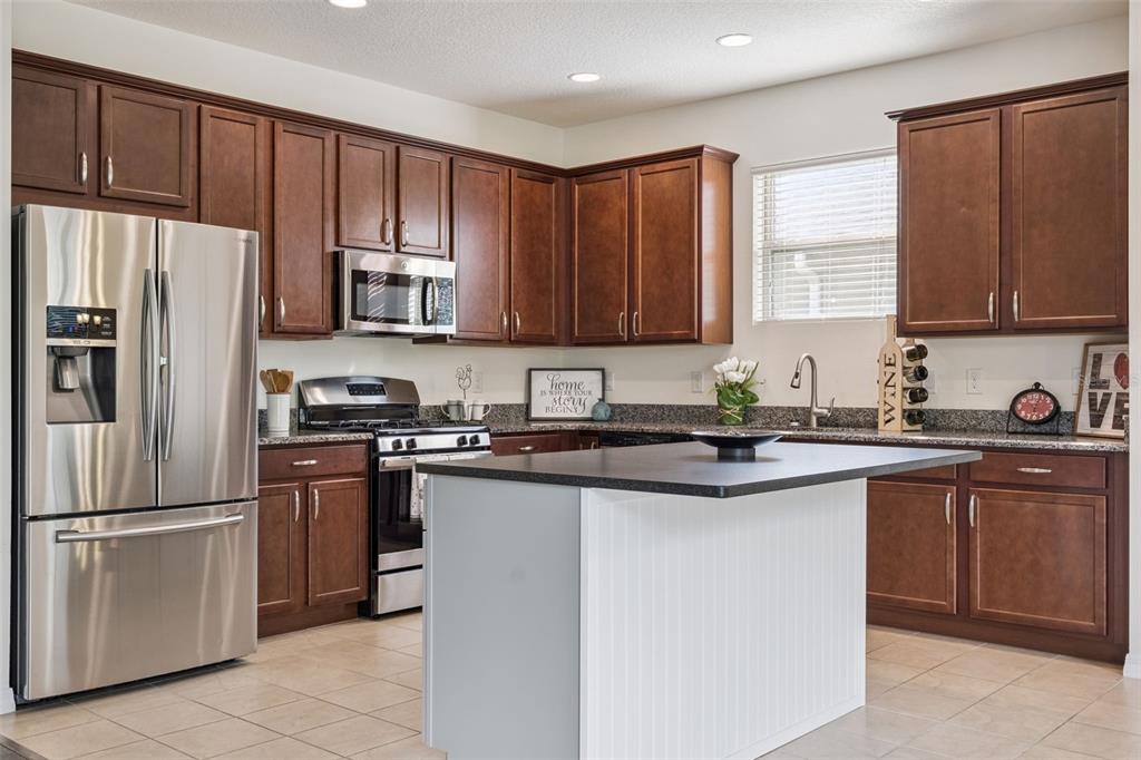 A kitchen featuring dark wood cabinets, stainless steel appliances, granite countertops, and a white island — 1013 SADIE RIDGE ROAD, CLERMONT, FL