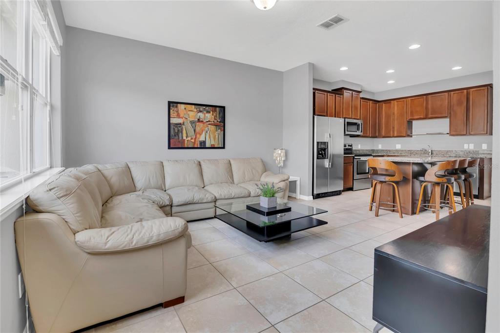 A living room with a beige sectional sofa and glass coffee table opens to a kitchen — 7752 RIGBY STREET, WINDERMERE, FL