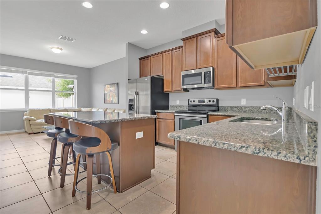 A kitchen with brown cabinets, granite countertops, stainless steel appliances, and an island with stools — 7752 RIGBY STREET, WINDERMERE, FL