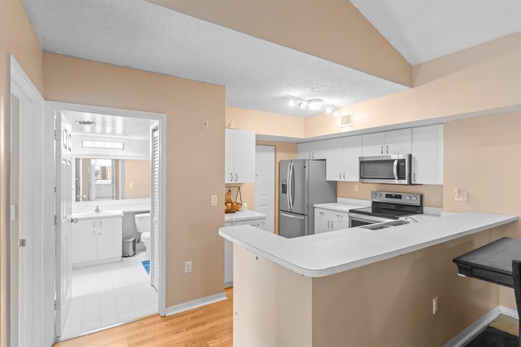 A kitchen with white cabinets and stainless steel appliances overlooks a breakfast bar and bathroom — 3874 Lyons Road # 6, Coconut Creek FL 33073, COCONUT CREEK, FL