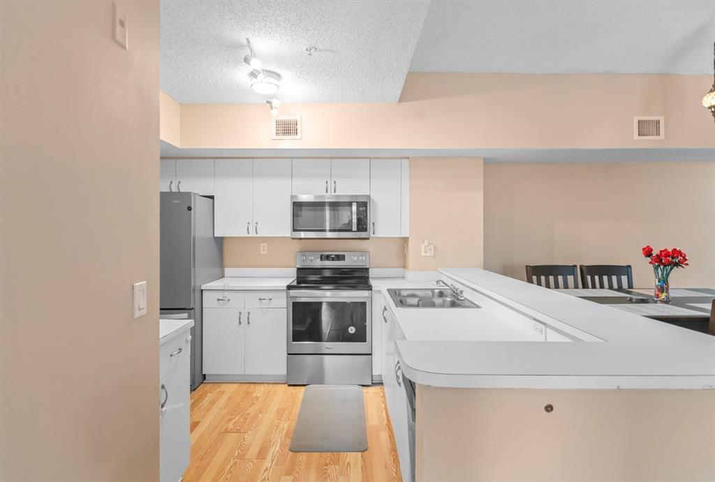 A kitchen features white cabinets, stainless steel appliances, and a breakfast bar with wood flooring — 3874 Lyons Road # 6, Coconut Creek FL 33073, COCONUT CREEK, FL