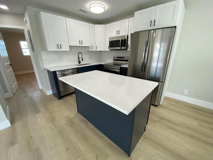A kitchen features white upper cabinets, dark blue lower cabinets, a central island, and stainless appliances — 332 Walton Boulevard, West Palm Beach FL 33405, WEST PALM BEACH, FL