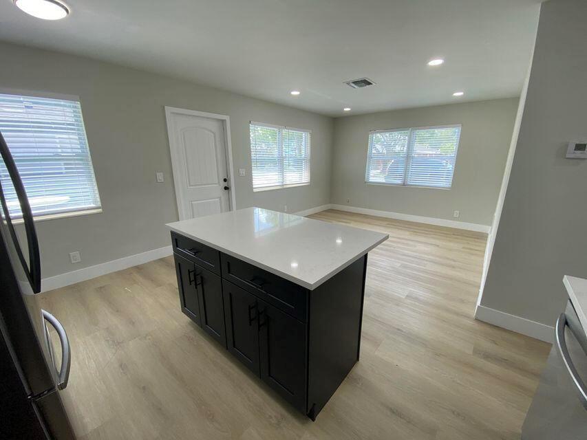 A kitchen island with a white countertop sits in a room with light wood flooring — 332 Walton Boulevard, West Palm Beach FL 33405, WEST PALM BEACH, FL
