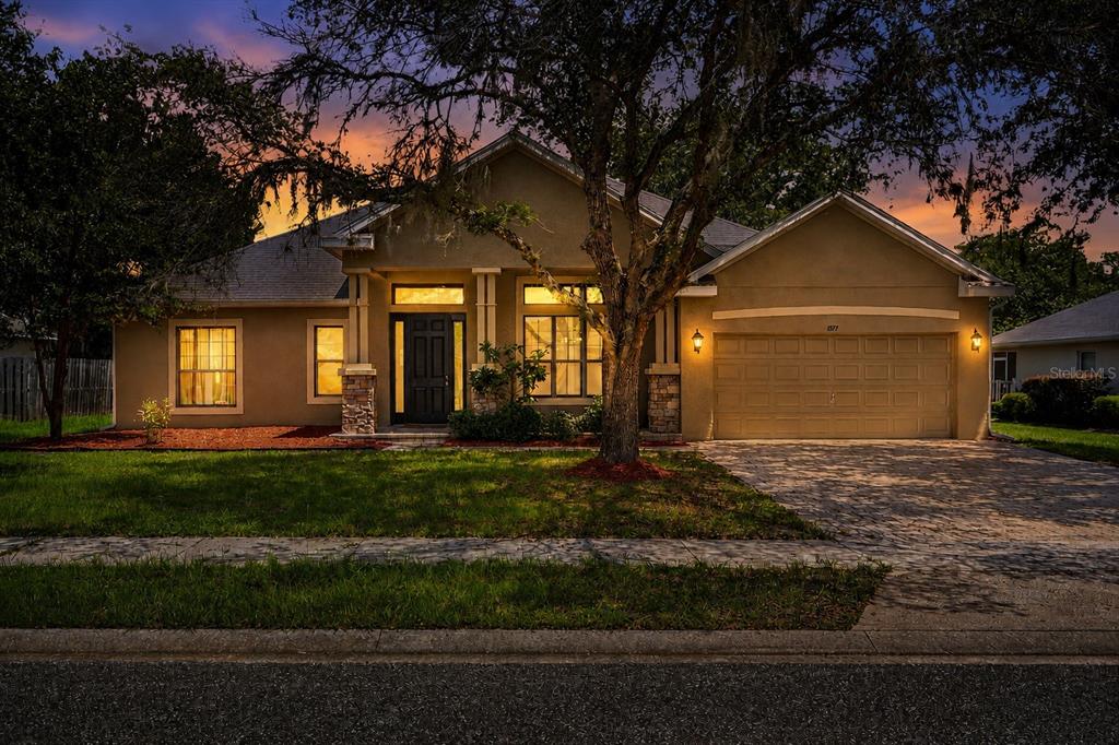 A single-story house with a tan stucco exterior, stone accents, and a two-car garage at dusk — 1517 CLAPTON DRIVE, DELAND, FL