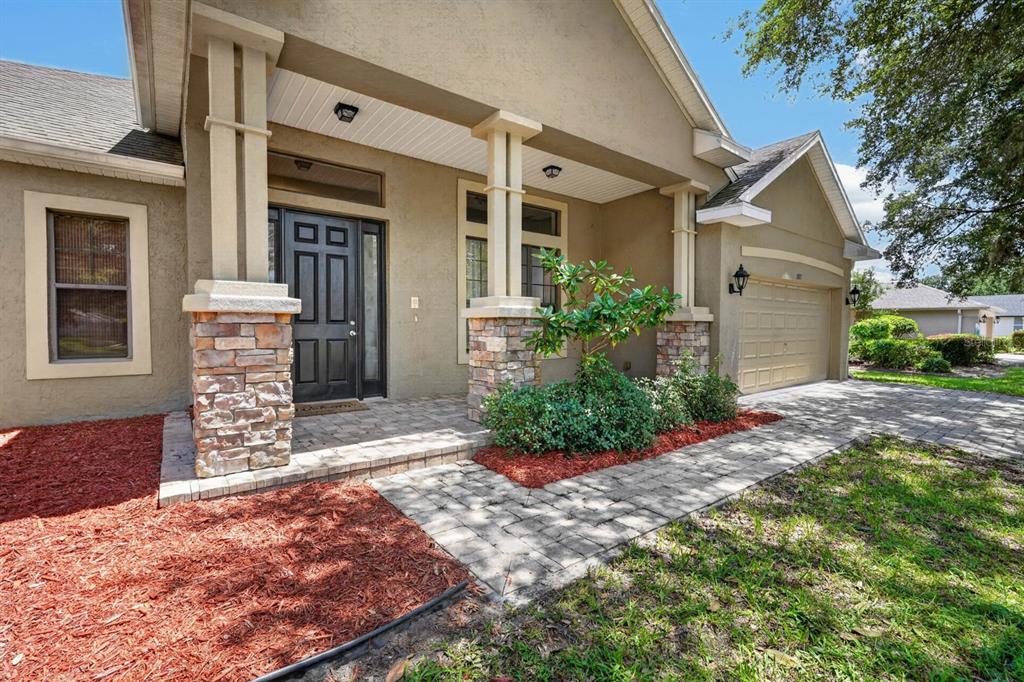 The exterior of a single-story house features a stone-accented porch, a paved walkway, and a garage — 1517 CLAPTON DRIVE, DELAND, FL